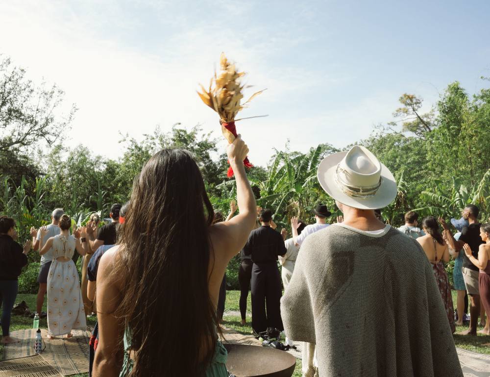 Guests raise their hands during an outdoor ceremony among banana trees at ChoZen
