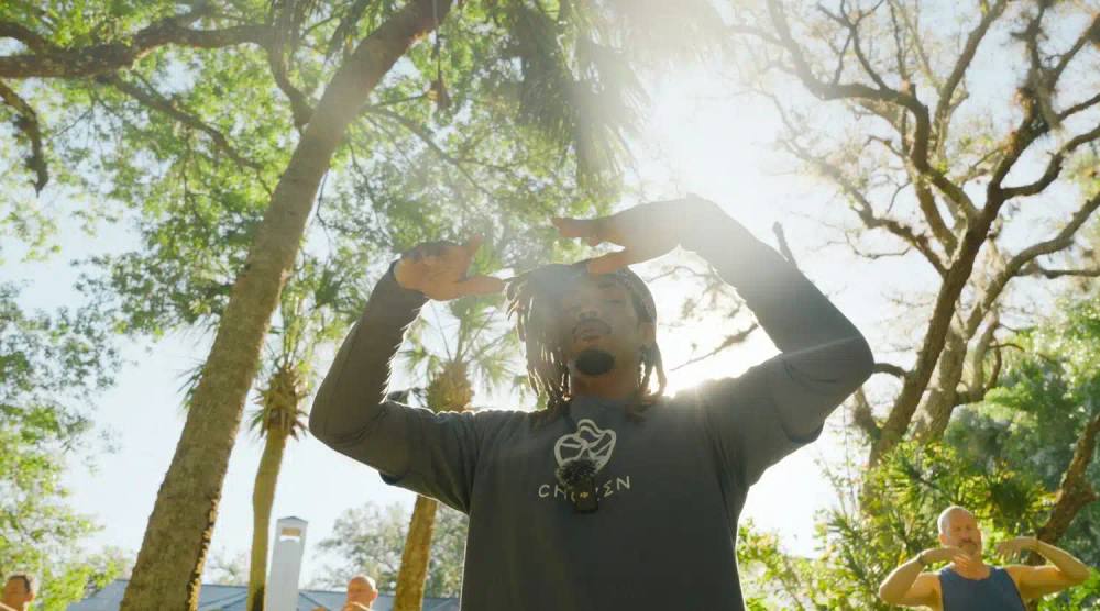 Instructor in a ChoZen shirt leading a sunlit outdoor flow movement class beneath palms